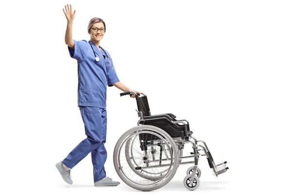 Полнометражный Снимок Молодой Медсестры Толкающей Пустое Инвалидное Кресло Машущей Изолированным — стоковое фото
