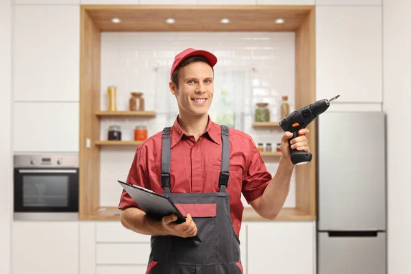 Repairman holding a clipboard and a drill machine in a kitchen