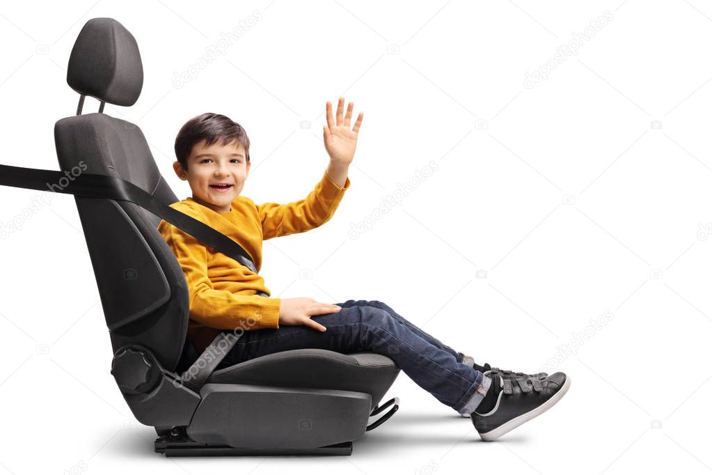 Full length shot of a little boy in a car seat with a fastened seatbelt looking at the camera and waving isolated on white background