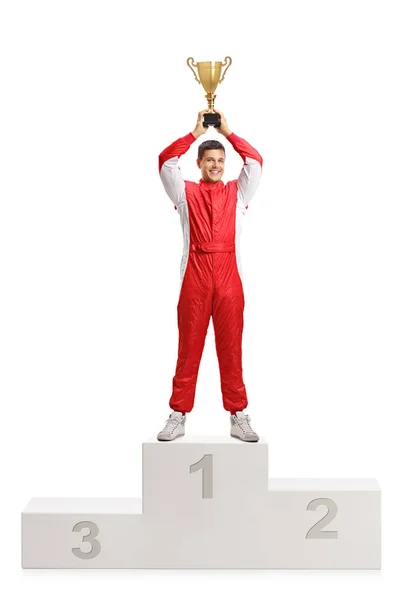 ゴールド トロフィーを持って 白い背景に分離された受賞者の台座の上に立っている男性の車のレーサーのフルの長さの肖像画 — ストック写真