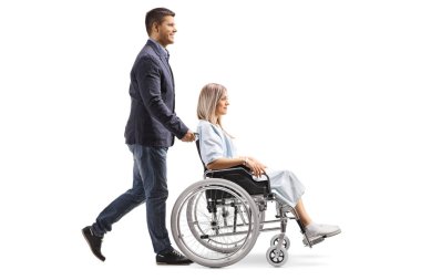 Genç bir kadın beyaz arka plan üzerinde izole tekerlekli sandalyede iterek bir gencin tam uzunlukta profil vurdu