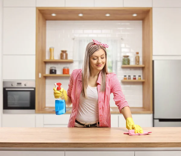 Young woman cleaning a wooden counter top in a kitchen