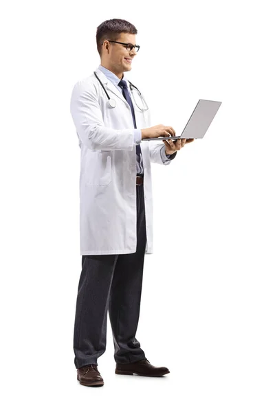 立っていると 白い背景で隔離のラップトップ コンピューターに入力 若い男性医師の全身ショット — ストック写真