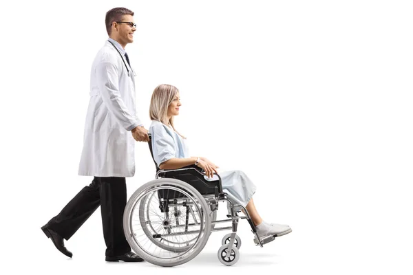 白い背景に分離された車椅子の女性患者を押す若い男性医師の全身ショット — ストック写真