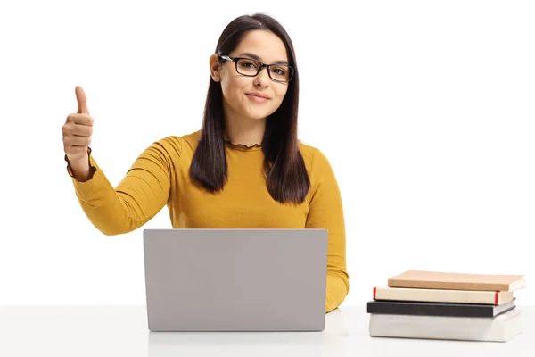 ノート パソコンと親指に分離の白い背景を示して本とテーブルに座って若い女性 — ストック写真