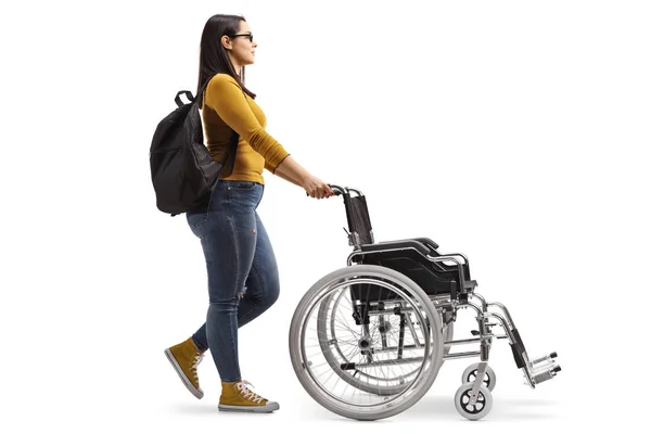 白い背景に分離された空の車椅子を押す女性学生の完全な長さのプロファイル ショット — ストック写真