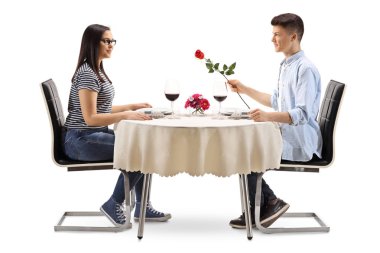 Tam uzunlukta profil bir restoran masada genç bir kadın bir gül veren bir genç erkek beyaz arka plan üzerinde izole