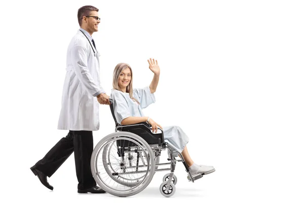 完全な長さに分離の白い背景を振って車椅子の女性患者を押す若い男性医師のショット — ストック写真