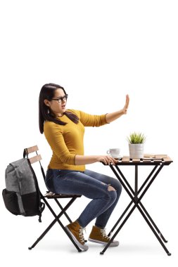 Kızgın bir kız öğrencinin bir kafede kahve ve el durağı ile beyaz arka plan üzerinde izole el ile bir masada oturuyor, tam uzunlukta profil vurdu