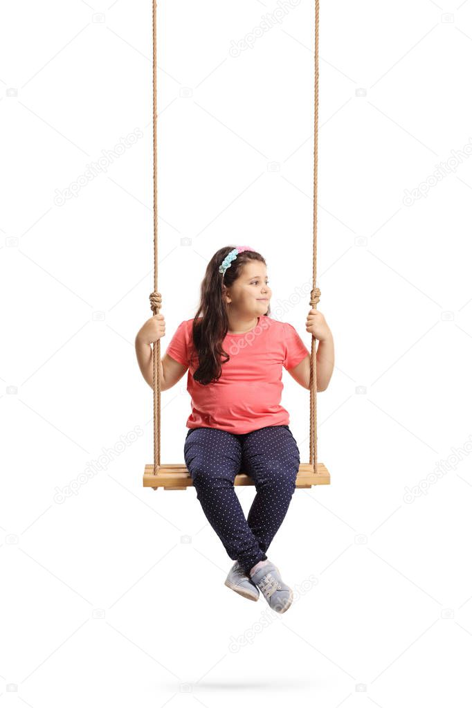 Full length shot of a little girl sitting on a swing and looking to the side isolated on white background