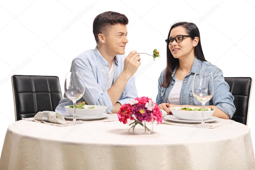 Young boyfriend giving a salad to his girlfriend at a restaurant table isolated on white background