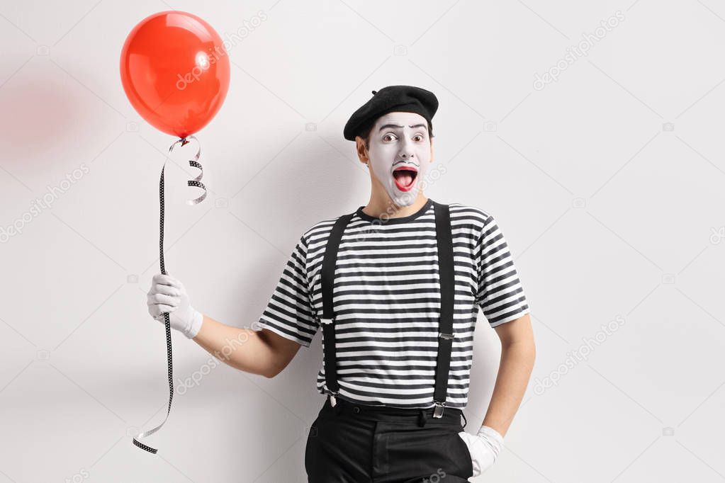 Mime holding a red balloon and leaning against a wall