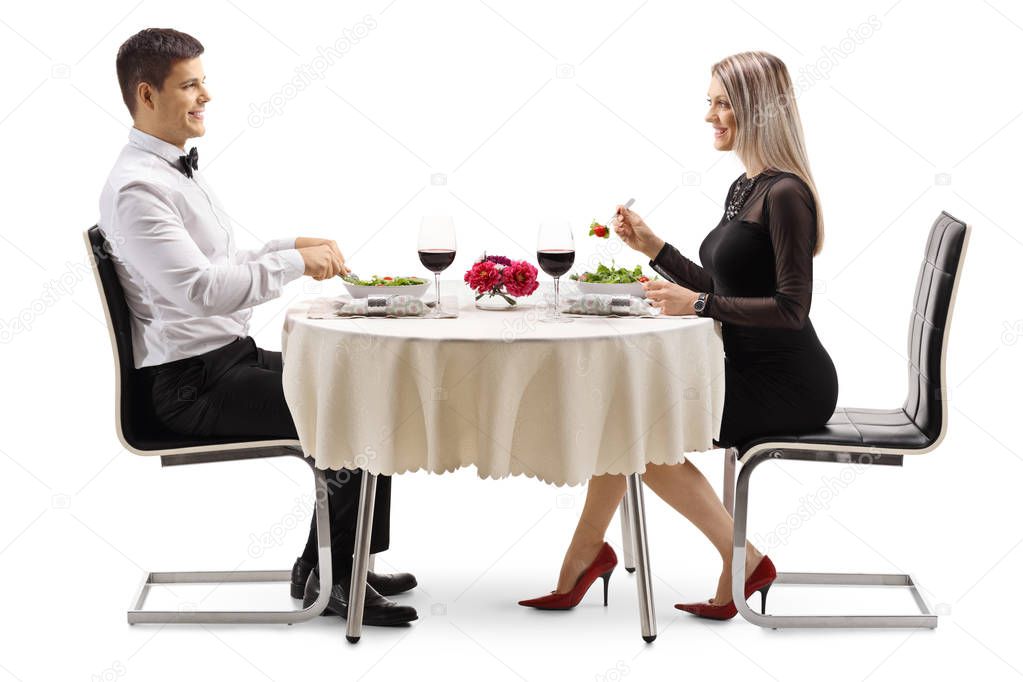 Full length profile shot of a young man and woman eating salad at a table isolated on white background