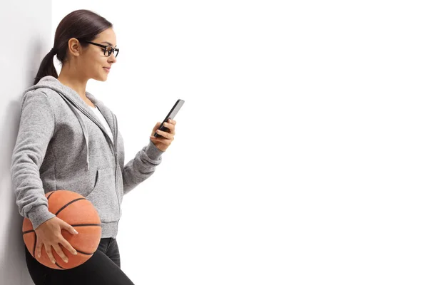 バスケットボールを壁にもたれ 白い背景に孤立した携帯電話を使用している若い女性 — ストック写真