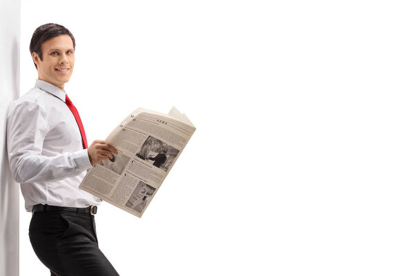 Professional young man with a newspaper leaning against a wall isolated on white background