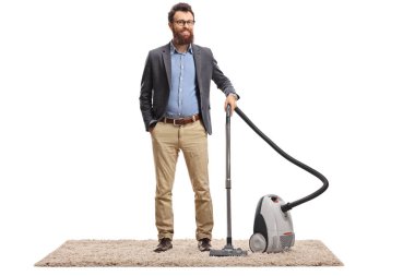Genç sakallı bir adam halının üzerinde elektrikli süpürgeyle poz veriyor.