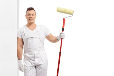 Beyaz arka planda izole edilmiş bir duvara yaslanmış boya silindirli genç bir ressam.