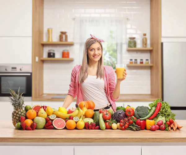 オレンジジュースと果物や野菜の山のあるキッチンで若い女性 — ストック写真