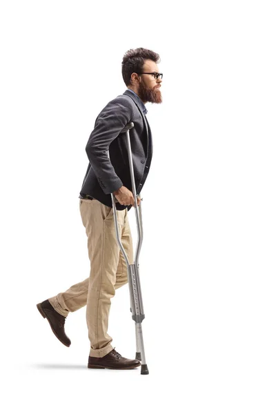 白い背景に隔離された松葉杖で歩いている若いあごひげの男の完全な長さのプロフィールショット — ストック写真