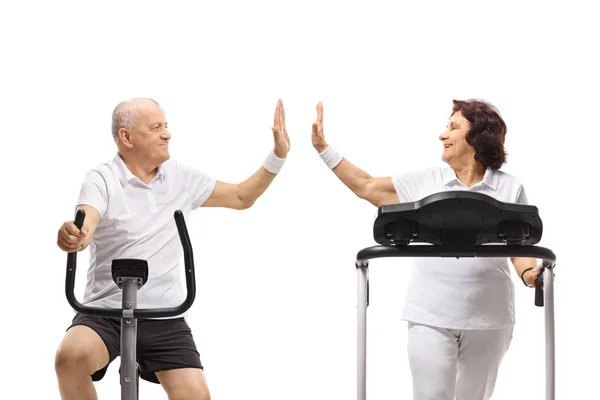 骑着固定自行车的老年男子和一位在跑步机上高飞的老年女子在白色背景上互相隔离 — 图库照片