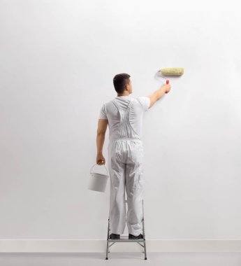 Beyaz arka plan üzerinde izole bir merdiven üzerinde bir duvar boyama bir adamın arka görünümü