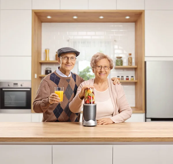 Senior man and woman in a kitchen with a fruit in a blender and a glass of fruit juice