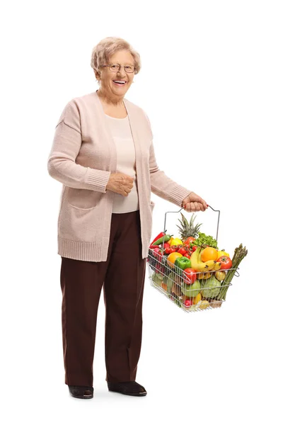白い背景に孤立した食料品の完全な買い物かごを持つ笑顔のシニア女性の完全な長さの肖像画 — ストック写真