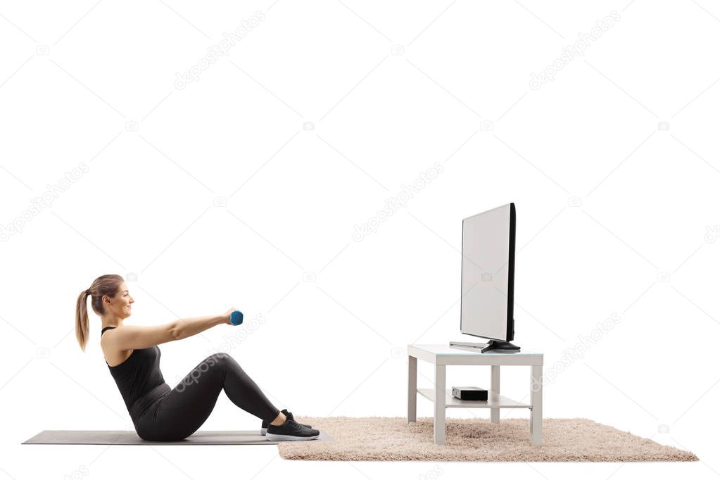 Young woman exercising with dumbbells infront of a TV at home isolated on white background