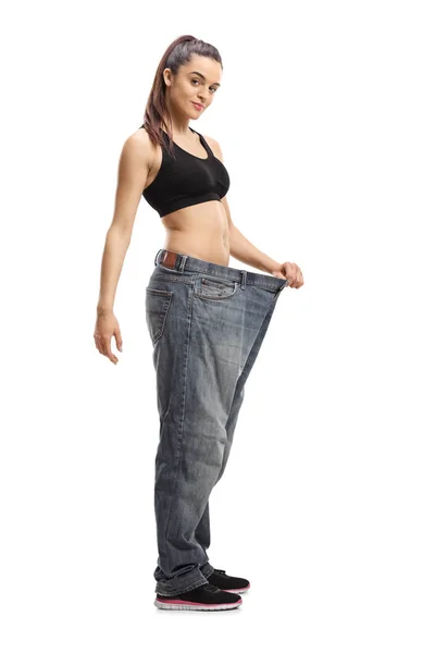 白い背景に隔離された減量後のジーンズの大きなサイズのペアを着て満足のいく若い女性のフルレングスショット — ストック写真