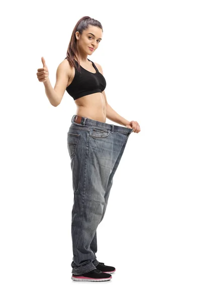 一个苗条的年轻女子穿着大尺寸牛仔裤的全长肖像显示竖起大拇指孤立在白色背景 — 图库照片
