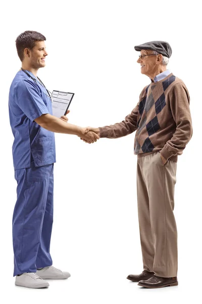 青い制服を着た男性医師が白い背景に孤立した先輩と握手する全長プロフィールショット — ストック写真