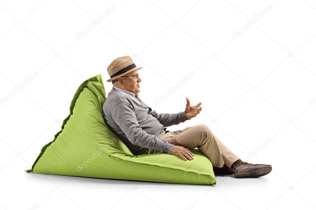 Full length shot of a senior man sitting on a bean-bag and gesturing with hand isolated on white background