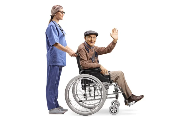 車椅子に座っている先輩を押し 白い背景に孤立した手で挨拶する女性看護師の全長プロフィールショット — ストック写真