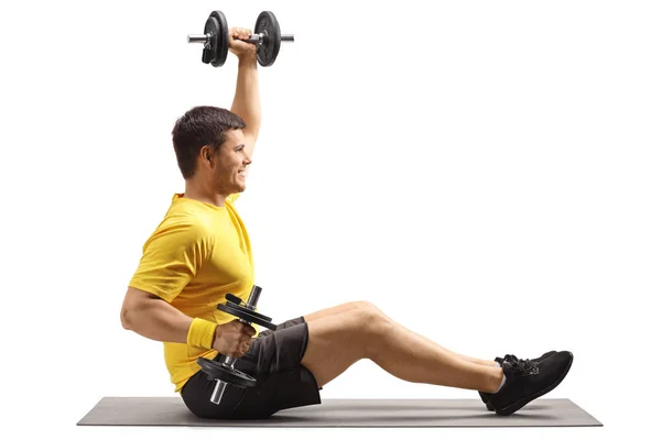 Junger Mann sitzt auf einer Gymnastikmatte und trainiert mit Hantel — Stockfoto