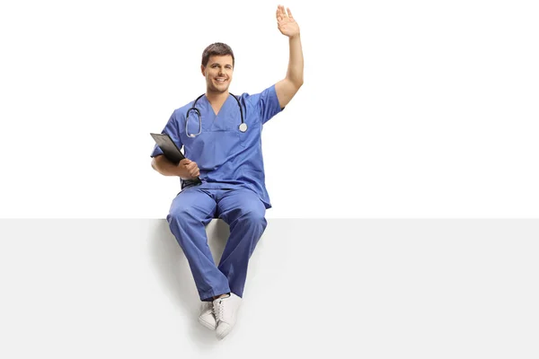 Young male doctor in a blue uniform sitting on a white panel and — Stock Photo, Image