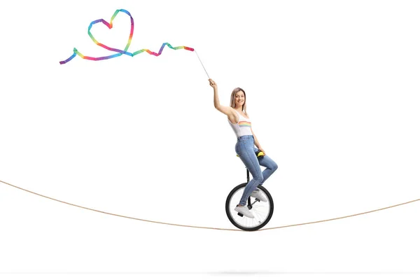Woman riding a unicycle on a rope and waving a ribbon with a hea — Stock Photo, Image