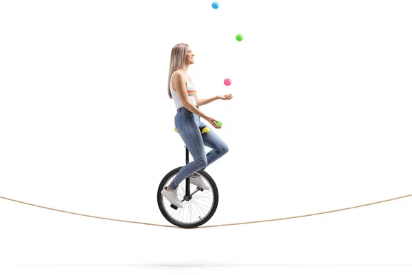 Молодая женщина катается на одноколесном велосипеде по веревке и жонглирует мячами — стоковое фото