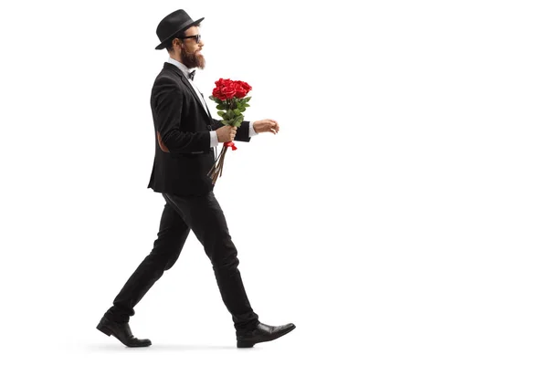 Ο άντρας με τα γένια σε ένα κουστούμι που περπατάει με ένα μάτσο κόκκινα τριαντάφυλλα — Φωτογραφία Αρχείου