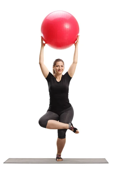 Jonge vrouw tilt een fitnessbal op en traint op een mat — Stockfoto