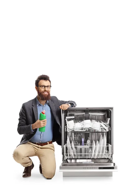Man knäböjer bredvid en diskmaskin och håller en flaska maskin — Stockfoto