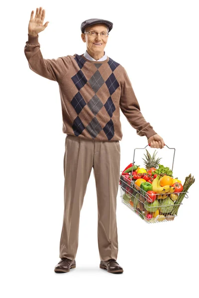 Senior man carrying a full shopping basket and waving at the cam — Stock Photo, Image