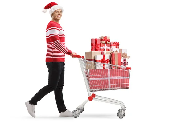 Young man with a shopping cart with presents wearing a santa hat — ストック写真