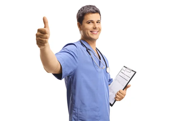 Νεαρός άνδρας γιατρός με μπλε στολή κρατώντας ένα πρόχειρο και δείχνοντας — Φωτογραφία Αρχείου