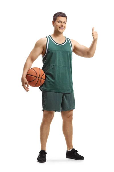 ボールを持ち 白い背景に孤立した親指を示すジャージを着た男性バスケットボール選手の全長の肖像画 — ストック写真