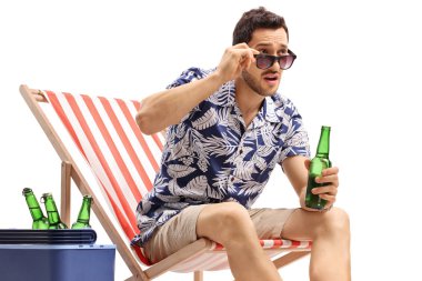Young guy with a beer bottle sitting in a deck chair and staring