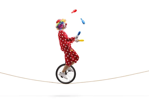 Clown juggling with clubs and riding a unicycle on a rope — Stock Photo, Image