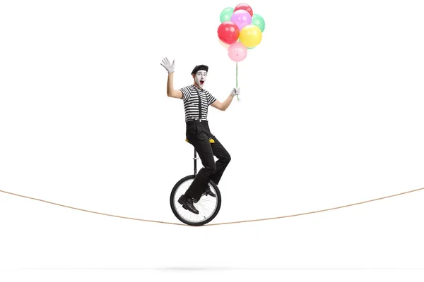 Mime riding a unicycle on a rope, holding a bunch of colorful ba — Stock Photo, Image