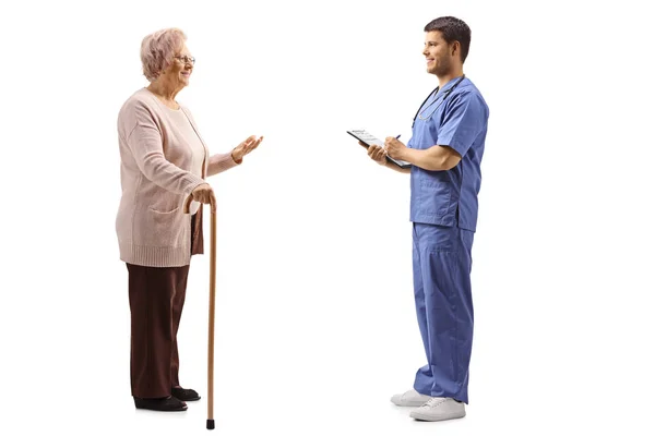 Старшая женщина разговаривает с молодым врачом-мужчиной в синей форме — стоковое фото