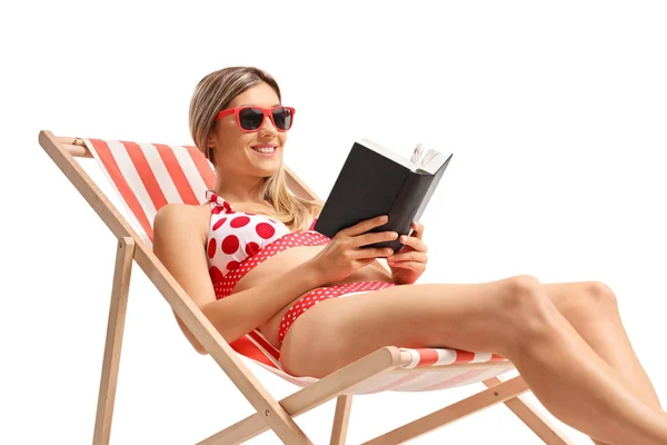 Ung kvinna i bikini läser en bok medan hon solar — Stockfoto