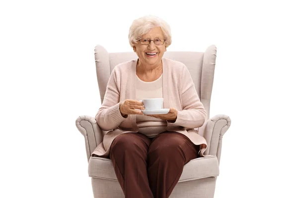Starsza kobieta trzyma filiżankę i siedzi na fotelu — Zdjęcie stockowe